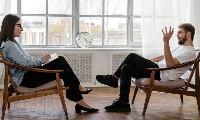 Rozmowa terapeutyczna we Wrocławiu. Kobieta z notatnikiem słucha mężczyzny, który opowiada o swoich problemach. Psychologia zaocznie Wrocław.
