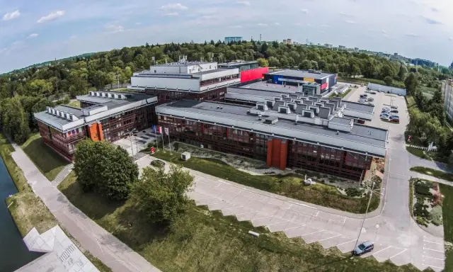 Nowoczesne budynki uczelni w Łodzi, otoczone zielenią, z widokiem na miasto.
