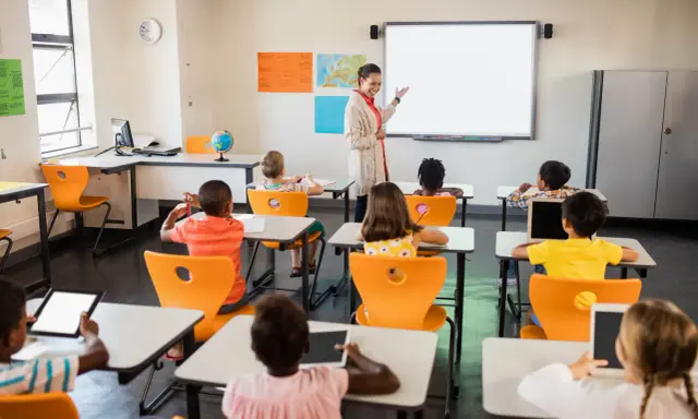 Nauczycielka prowadzi lekcję w klasie pełnej dzieci. To idealne miejsce do nauki pedagogiki przedszkolnej i wczesnoszkolnej w Poznaniu.