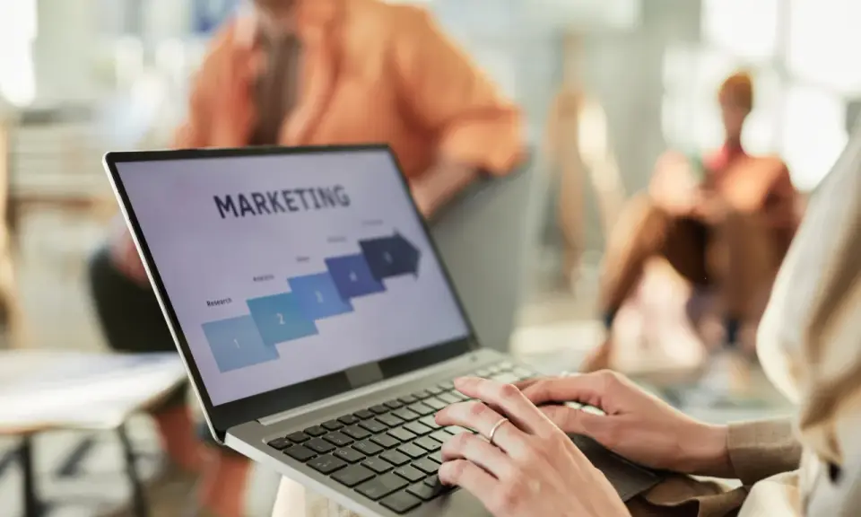 Osoba pracuje na laptopie z prezentacją "MARKETING". Widoczne etapy: Research, Analysis, Sales. Idealne do studiów zarządzanie i marketing.
