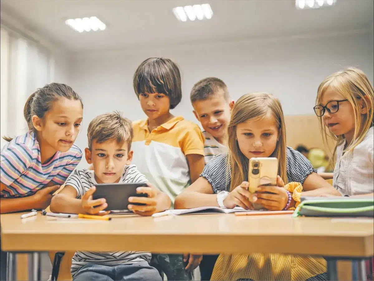 Dzieci pochylone nad telefonami, uczą się przez social media. Wszyscy skupieni na ekranach, widać zaciekawienie i zaangażowanie w cyfrowy świat.