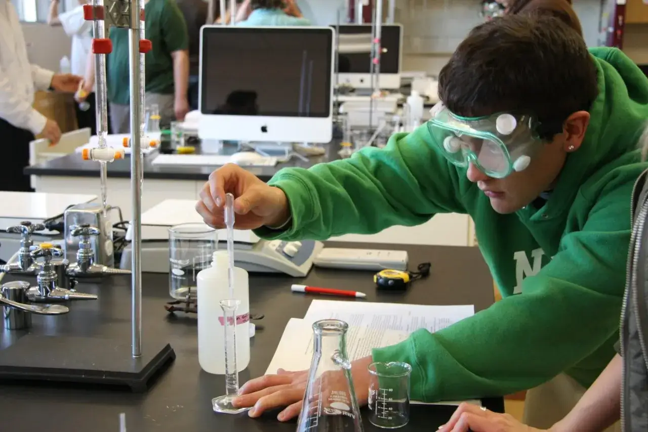 Uczeń w okularach ochronnych wykonuje doświadczenie chemiczne w pracowni wyższej szkoły technicznej.