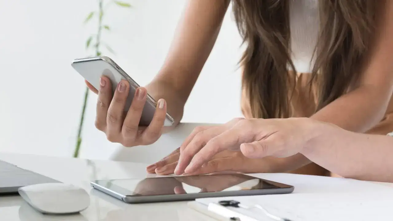 Dwie kobiety pracują nad aplikacją mobilną, jedna trzyma telefon, druga dotyka tabletu. Tester aplikacji mobilnych w akcji.