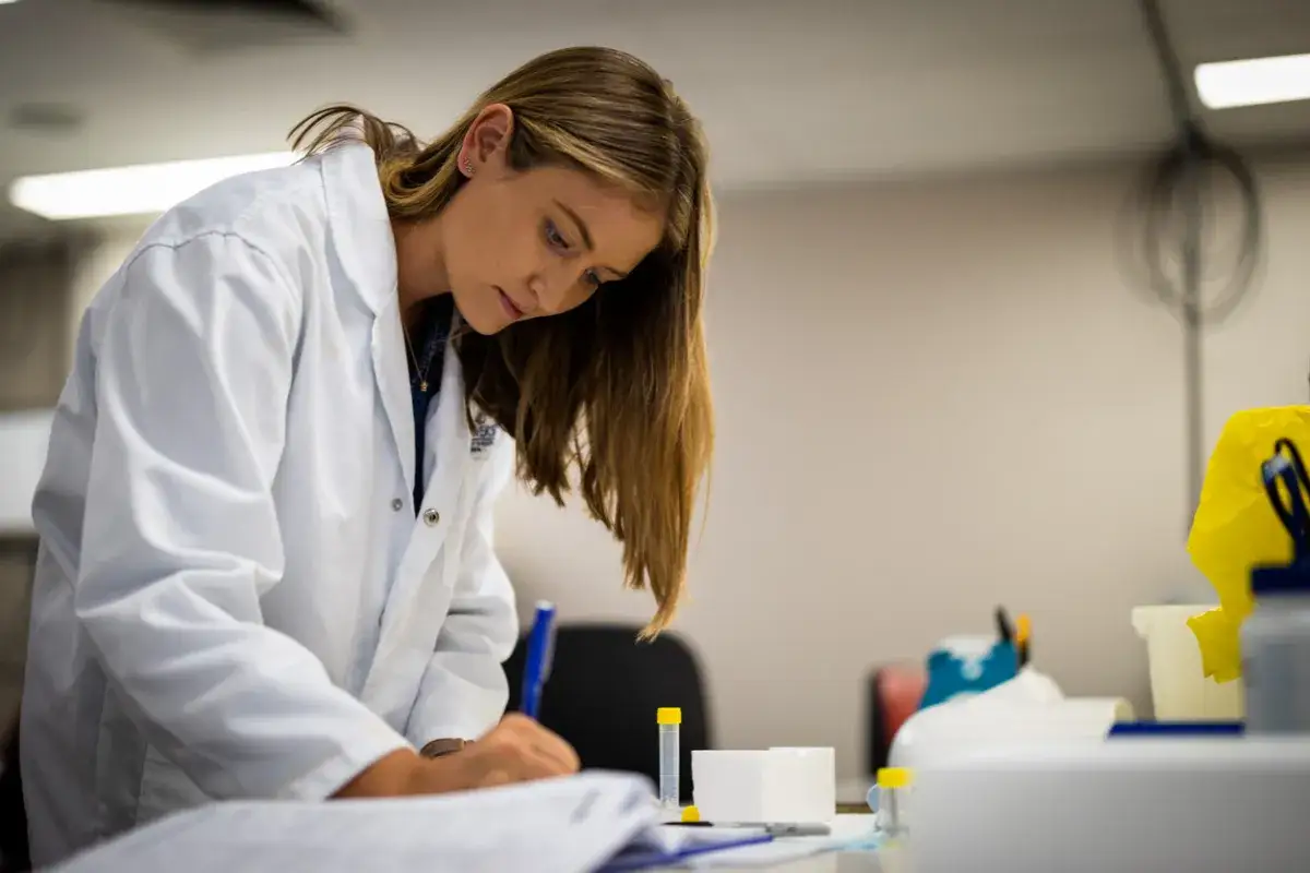 Studentka farmacji zaocznej w białym fartuchu notuje wyniki badań w laboratorium.