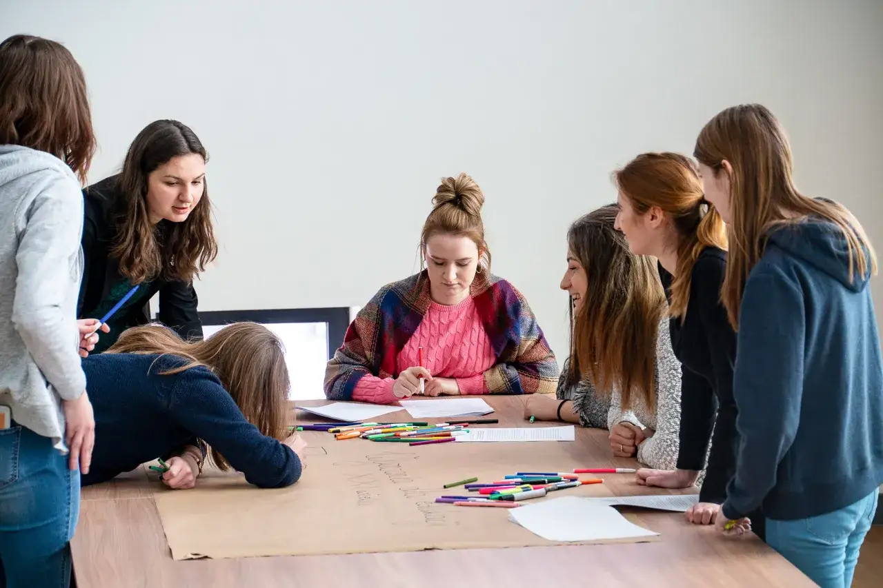 Studenci pracują nad projektem, dyskutując i notując. Tak wyglądają egzaminy na studiach, gdy liczy się współpraca i kreatywność.