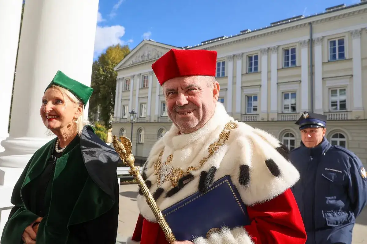 Uroczysta toga i biret wskazują, że to rektor a dziekan na tle uniwersyteckiego gmachu.