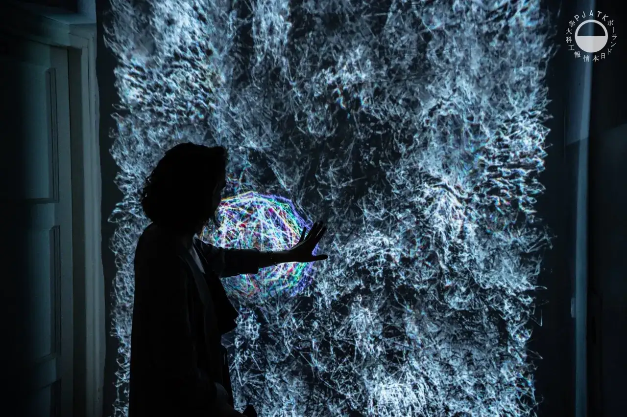 Sylwetka osoby wpatruje się w dynamiczną projekcję, która przypomina abstrakcyjne dzieło sztuki. To inspiracja dla projektowania graficznego studia, gdzie kreatywność nie zna granic.